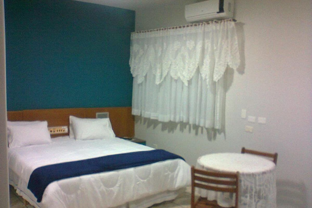 Une chambre d’hôtel comprenant un lit, une table de chevet, une chaise et un appareil de climatisation.