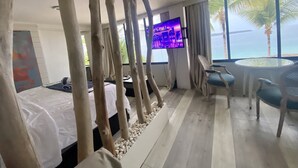 Camera d'albergo con un letto, una TV, un tavolo da pranzo con sedie e vista sul mare.