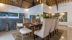 Un comedor con una mesa de madera, sillas acolchadas y techo de paja.
