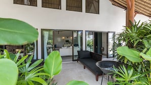Un espacio exterior moderno con zona de estar, sofá y mesa, rodeado de exuberante vegetación.