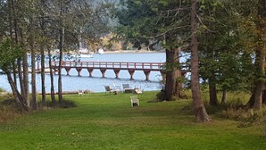 A grassy area with a wooden bridge over a body of water, surrounded by trees. -  San Juan Island Beach House, Waterfront Lodging just minutes from Roche Harbor! (Friday Harbor)