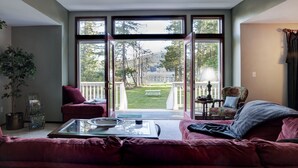 A living room with a large sliding glass door leading to a balcony, a sofa, a coffee table, and a chair. -  San Juan Island Beach House, Waterfront Lodging just minutes from Roche Harbor! (Friday Harbor)