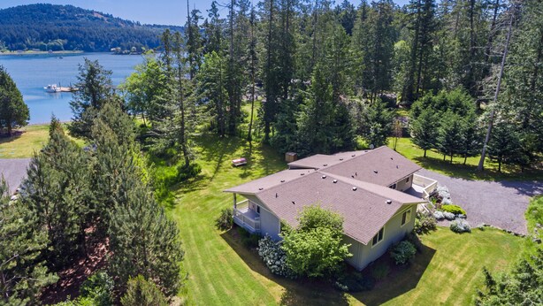 A two-story house with a sloped roof, surrounded by a well-maintained lawn and dense forest. -  San Juan Island Beach House, Waterfront Lodging just minutes from Roche Harbor! (Friday Harbor)