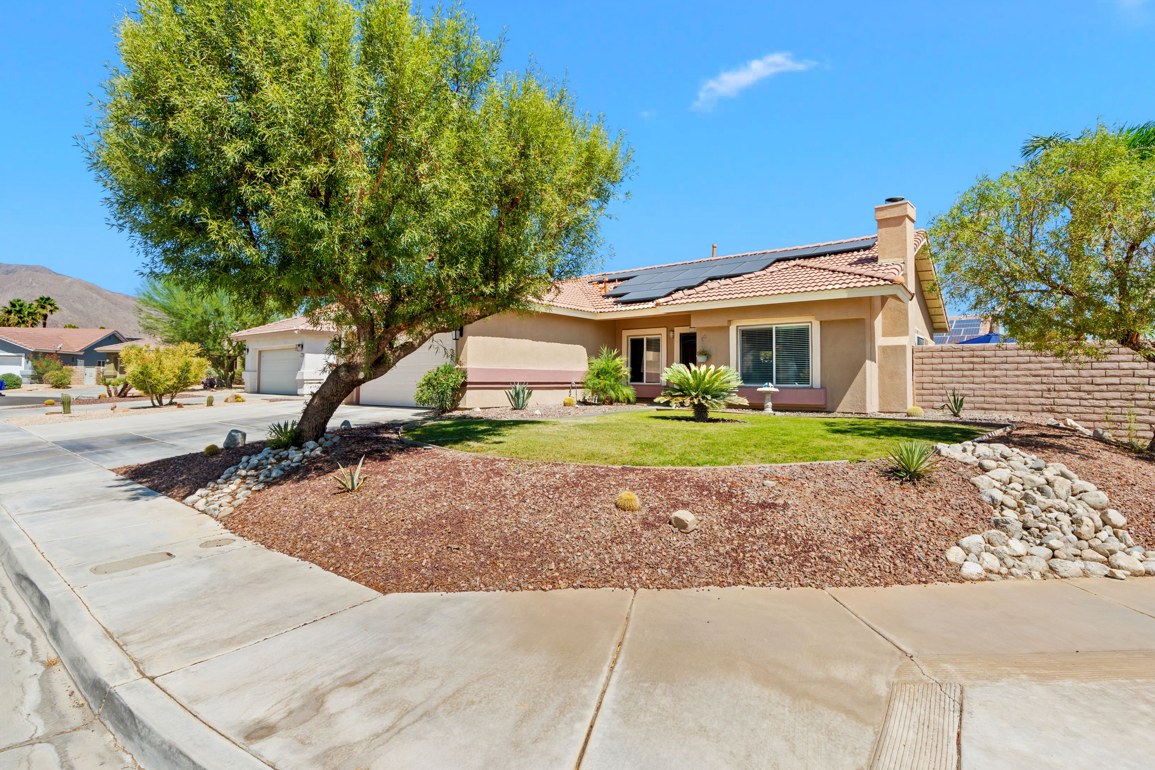 A residential house with a sloped roof, solar panels, a well-maintained lawn, and a stone pathway leading to the entrance.