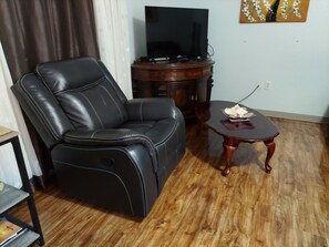 A living room with a leather sofa, a wooden coffee table, and a flat-screen TV on a wooden stand. - Englewood Cozy Comfy Home  (Englewood)