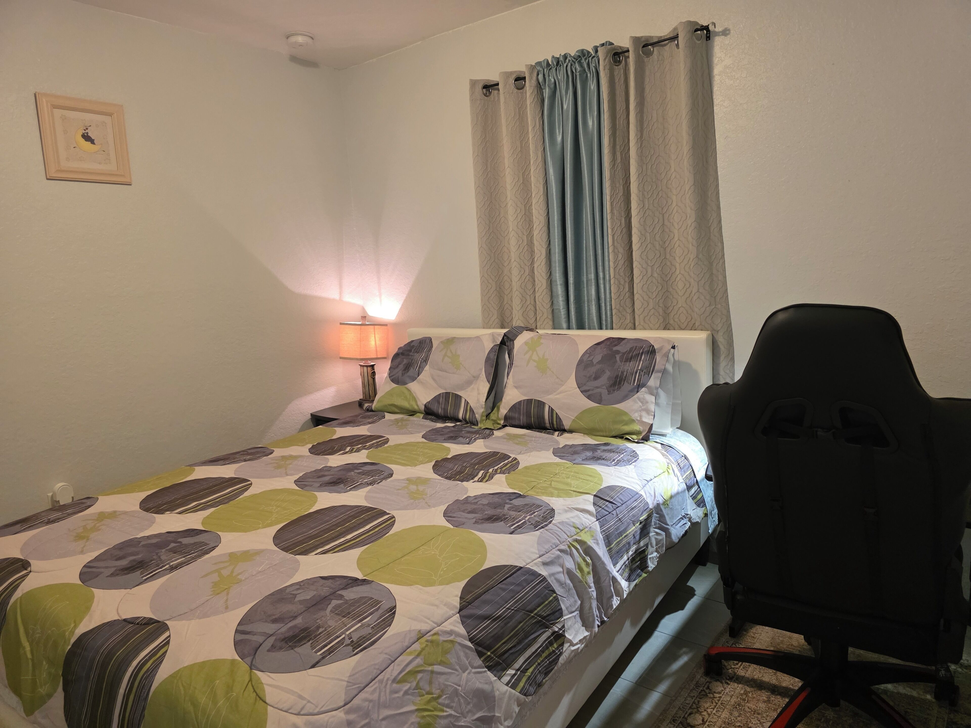 A bedroom with a bed, a desk, a chair, a lamp, and curtains.