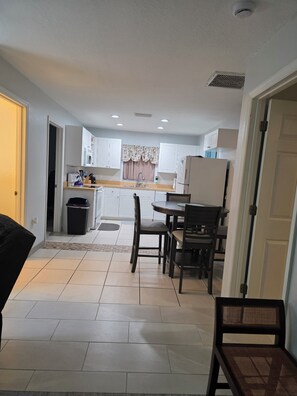 A compact kitchen with white cabinets, a dining table with chairs, and a black trash bin. - Englewood Cozy Comfy Home  (Englewood)