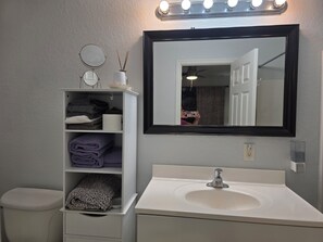 A bathroom with a white sink, a mirror, and a shelf with folded towels. - Englewood Cozy Comfy Home  (Englewood)