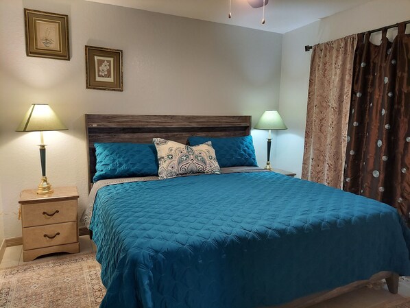 A bedroom with a large bed, two bedside tables with lamps, a wooden headboard, and two framed pictures on the wall.