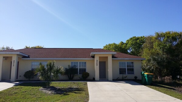 A two-story house with a red-tiled roof, beige walls, and a front yard with a small palm tree and a green trash bin. - Englewood Cozy Comfy Home  (Englewood)