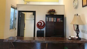 Un'area reception con una scrivania in legno, una ventola a soffitto, una libreria con libri, una spirale decorativa e un orologio a parete.