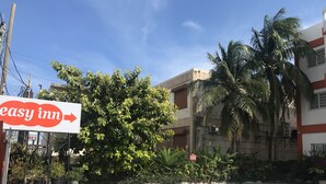 Segnaletica per 'easy inn' con una freccia direzionale, circondata da vegetazione e un edificio con numerose finestre.