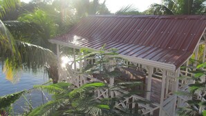 Una estructura de madera con techo de metal, rodeada de abundante vegetación y palmeras.