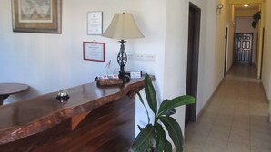 Un área de recepción con un mostrador de madera, un reloj, certificados enmarcados y una lámpara.