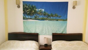 Una habitación con dos camas, una mesita con una lámpara y un tapiz con motivo de playa en la pared.