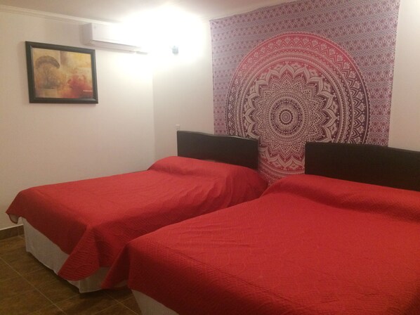 A room with two single beds, a tapestry, a framed picture, and a white air conditioning unit.