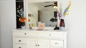 Et hvidt toiletbord med et spejl, to vaser med blomster, en lampe og nogle toiletartikler.