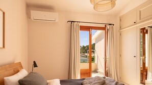 Ein Schlafzimmer mit einem Bett, einem Nachttisch, einer Klimaanlage, einem Fenster mit Vorhängen und Blick ins Freie.