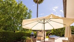 Eine Terrasse im Freien mit einem Holztisch und Stühlen, einem großen Sonnenschirm und einem Grill.