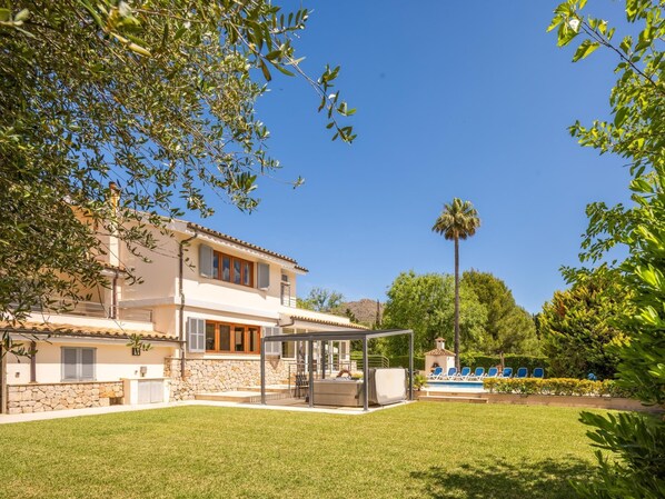 Une maison à deux étages avec une façade en pierre, un patio couvert et une piscine équipée de chaises longues.