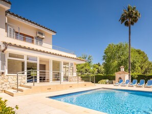 A two-story building with a swimming pool, outdoor seating, and a palm tree.