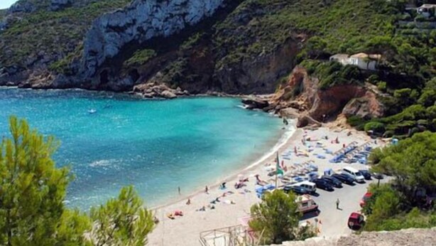 A beach with clear turquoise water, a sandy shore, and parked cars. - 3 bed 2 bath family villa, close to beach, Smart TV, WIFI and air con (Javea)