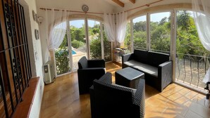 A sunlit room with a large sliding glass door leading to a pool, furnished with black wicker furniture and a wooden ceiling. - 3 bed 2 bath family villa, close to beach, Smart TV, WIFI and air con (Javea)