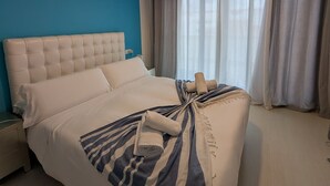 Una cama bien hecha con una manta a rayas y toallas enrolladas, un cabecero capitonado y una lámpara colgante.