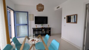 Una sala de estar moderna con una mesa de comedor de vidrio, sillas azules, un mueble de entretenimiento negro y un televisor.