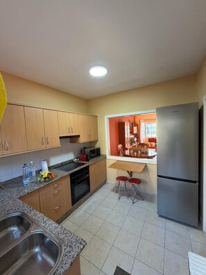 Una cocina con armarios de madera, un lavamanos de acero inoxidable, un microondas y un refrigerador.