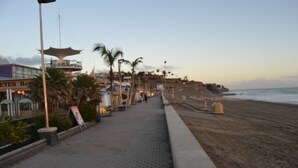 Un paseo marítimo con palmeras, una playa y un edificio con un letrero que dice 'EYES RE'.