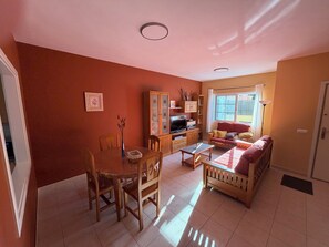Una sala de estar con una mesa de comedor, sillas, un sofá y un televisor.