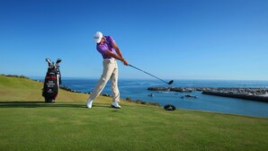 Un golfista en un campo de golf con vista despejada al océano y barcos en el fondo.