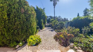 A cobblestone pathway leading through a garden with various plants and a palm tree in the distance. - Beautiful, Private Family Villa with Great Pool and access to Beaches, Mountains (Monte Canelas, Nr Alvor, District of Portimão)