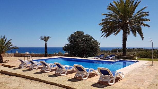 Ein Poolbereich mit Liegestühlen und Blick aufs Meer.