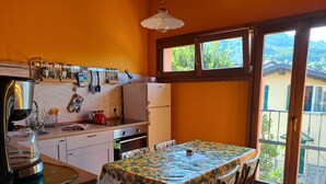 Cozinha com área de jantar, destacando uma mesa com toalha de mesa de girassol, armários de madeira e janela com vista para o verde.