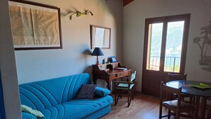 Quarto com sofá azul, secretária de madeira e cadeiras. Quadros emoldurados na parede e janela com vista.