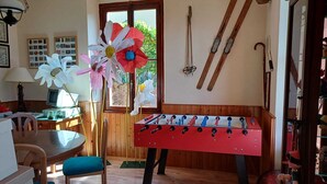 Quarto aconchegante com uma mesa de madeira, uma mesa de pebolim vermelha e uma janela com vista para o verde.