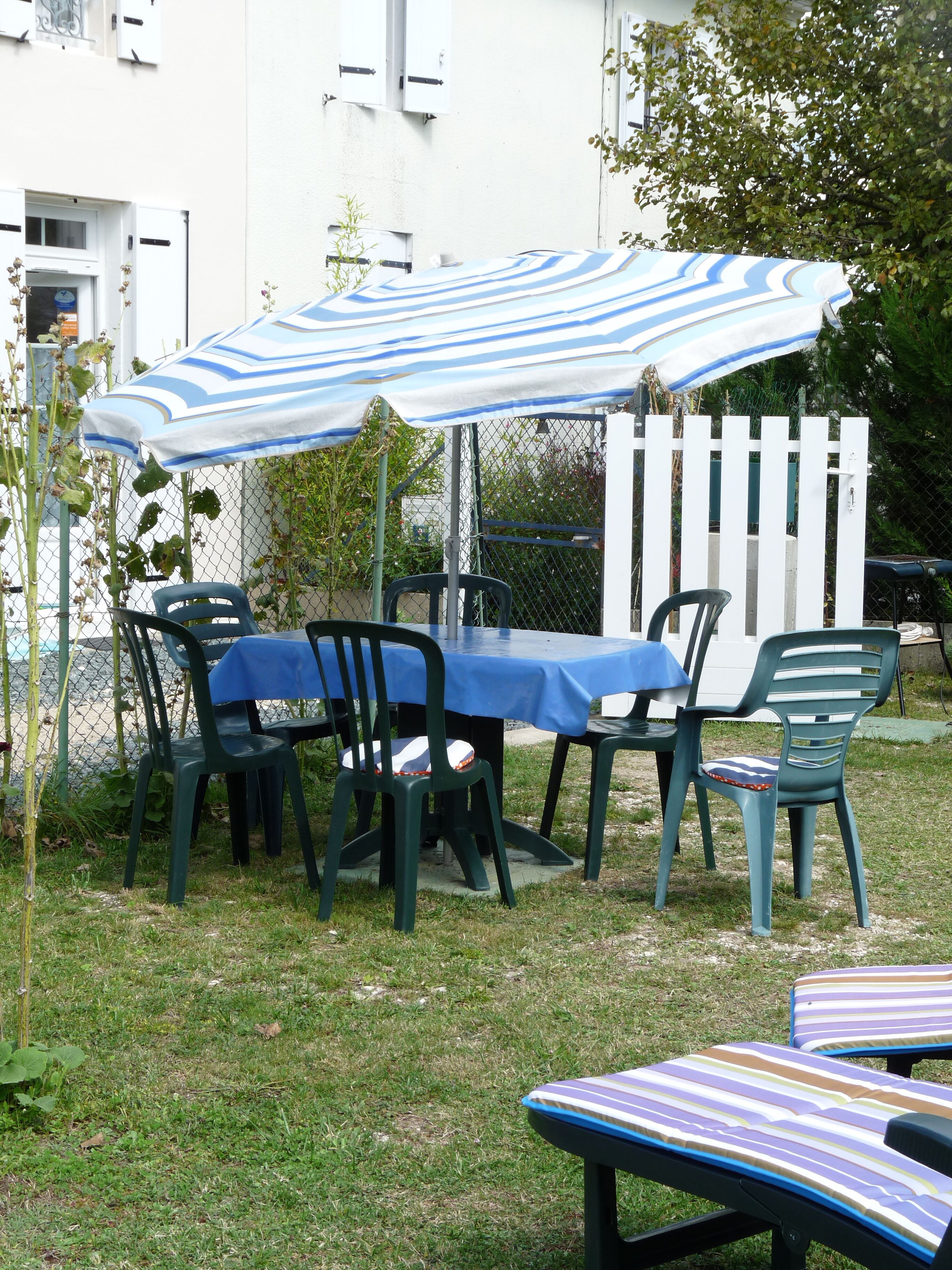 An outdoor patio with a table and chairs, a striped umbrella, and a white picket fence.