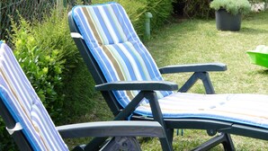 Due poltrone da relax a righe con struttura in metallo, collocate in un’area verde all’aperto con una recinzione in rete metallica e vegetazione sullo sfondo.