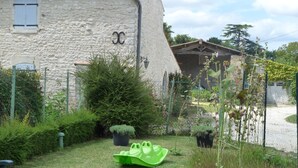 Un edificio in pietra con un camino, un piccolo giardino e una barca verde, il tutto delimitato da una recinzione.