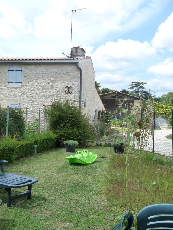 A stone building with a chimney, a small garden with a green boat, and a fence.