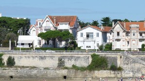 Un edificio sul lungomare con un balcone, un muro in pietra e una spiaggia in primo piano.