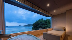 Een kamer met een bed, een jacuzzi en een groot raam met uitzicht op zee.
