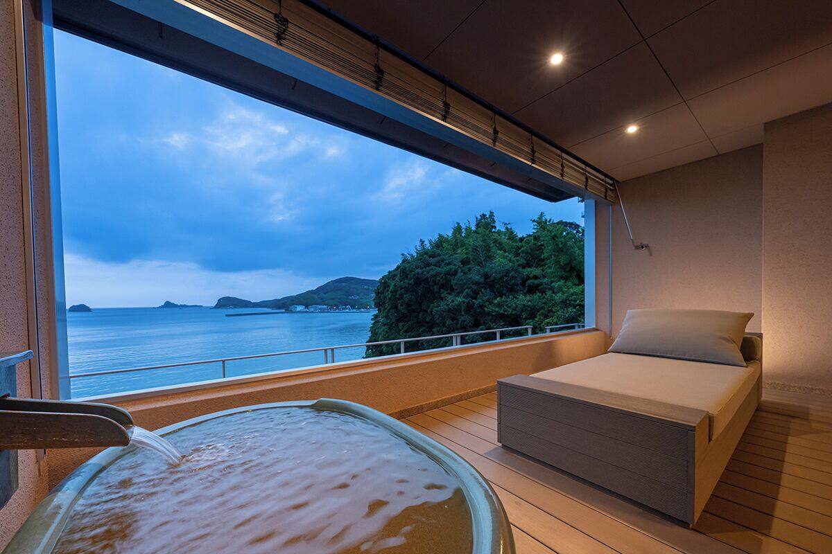Een kamer met een bed, een jacuzzi en een groot raam met uitzicht op zee.