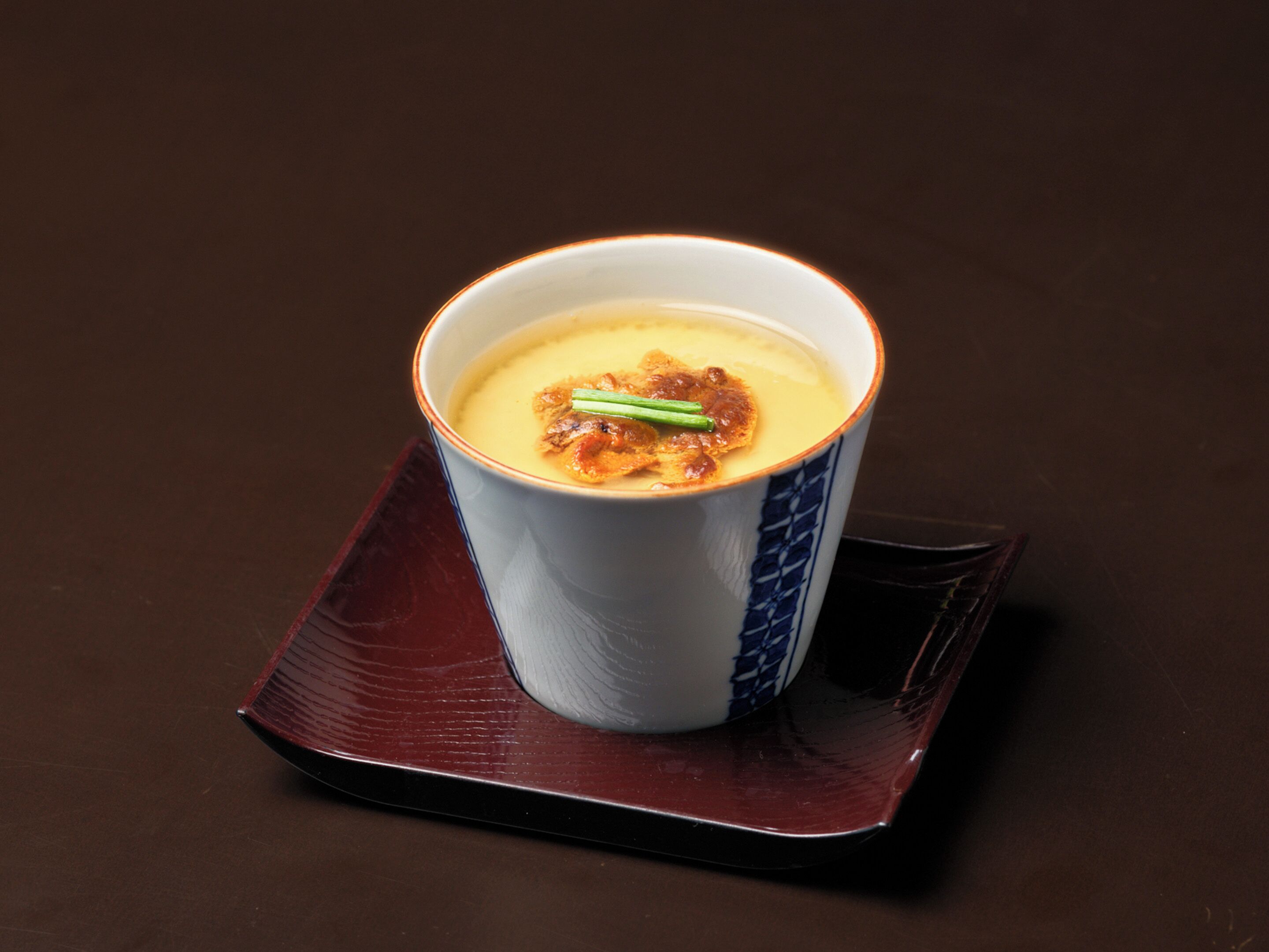 A cup of soup on a dark square plate.
