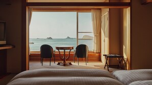 Een hotelkamer met een groot raam, een bed, een tafel met twee stoelen en een klein bureau.