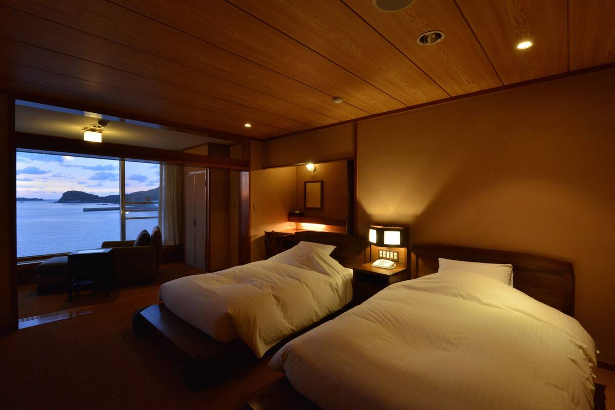 Een hotelkamer met twee bedden, een nachtkastje met lamp, een stoel en uitzicht op zee.