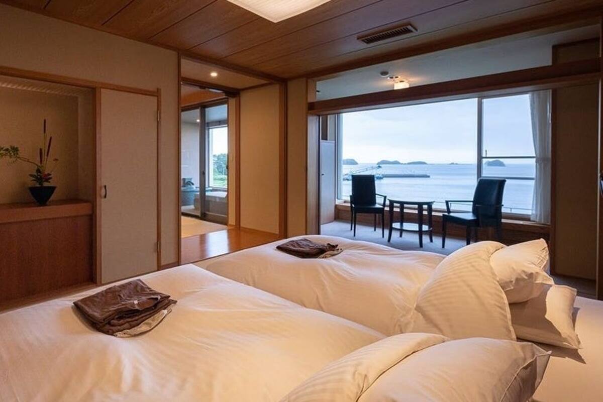 Een hotelkamer met twee bedden, een televisie, een plant in pot en uitzicht op zee.