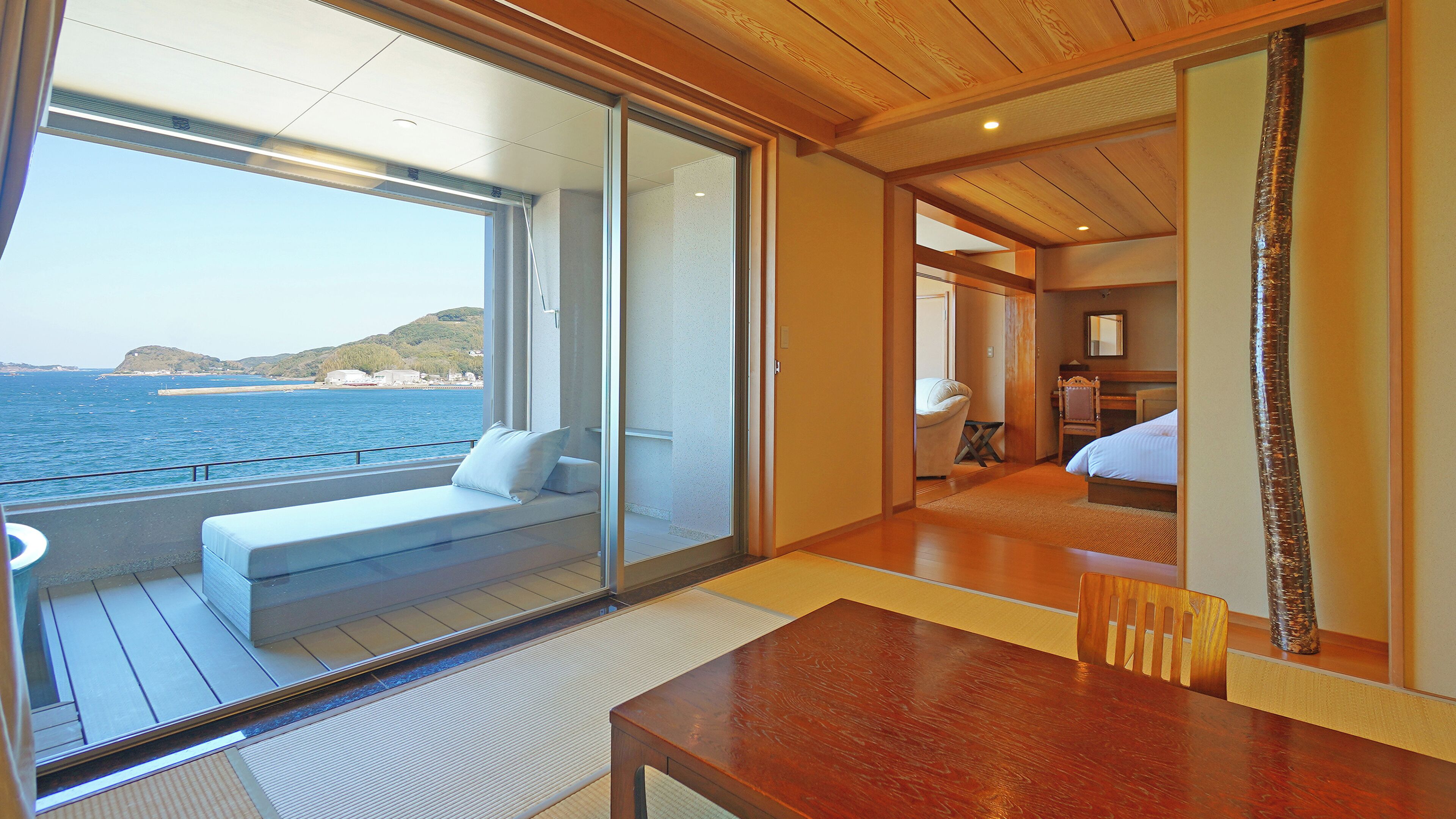 Una habitación con una mesa de madera, un sofá con un cojín, una cama y vistas al mar.